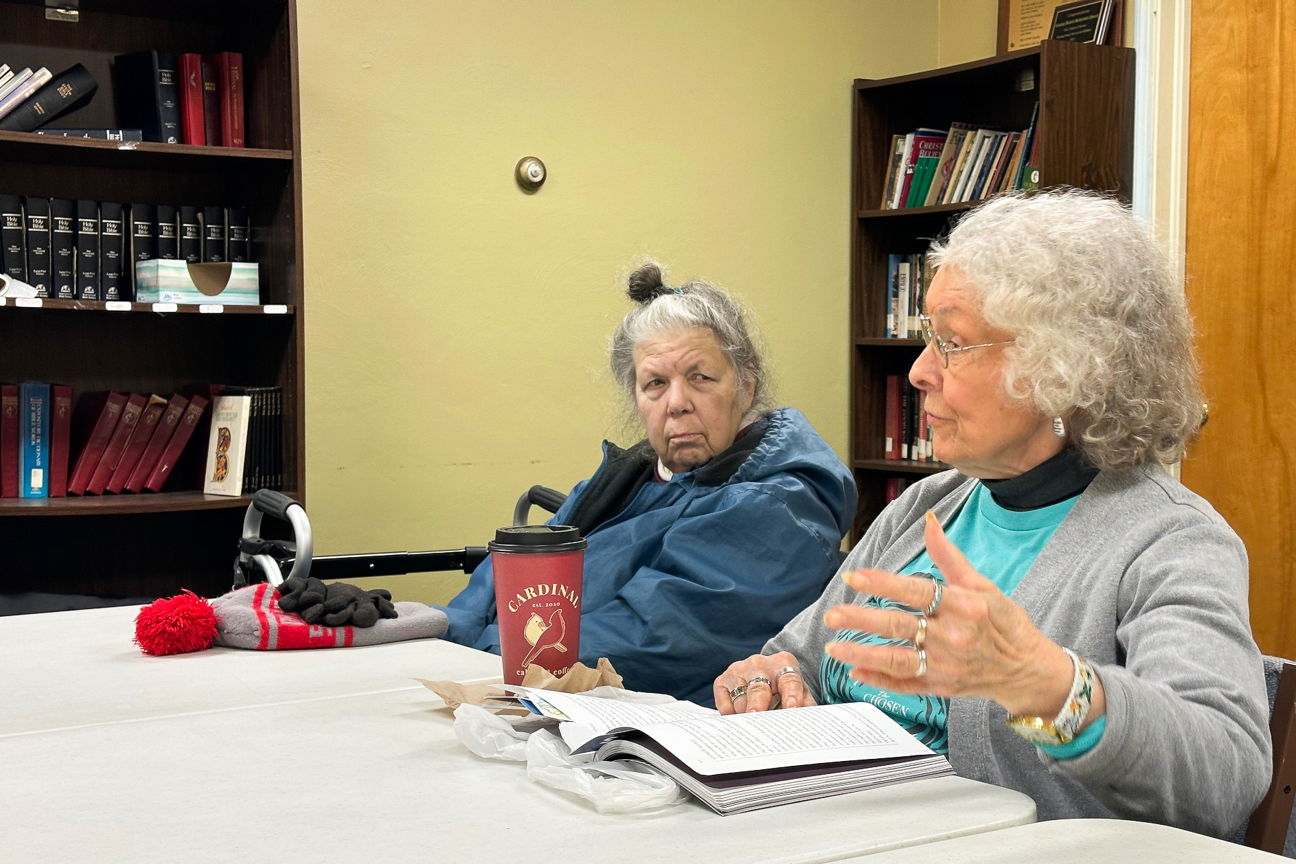 Two members of bible study having a discussion while one reads from a book.