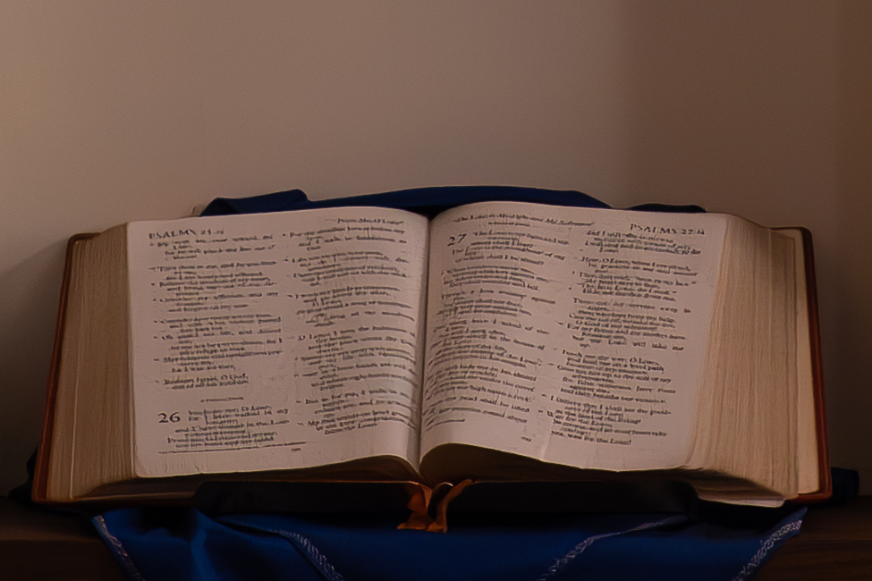 The bible open on a stand on top of blue draped fabric.