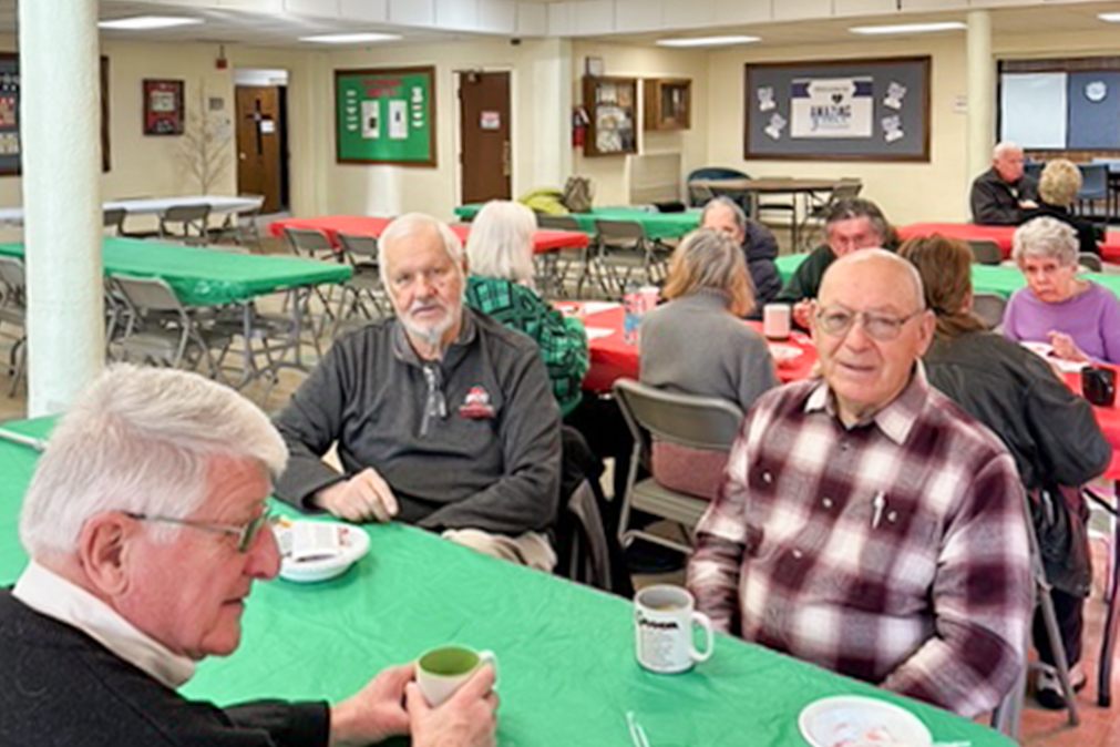 Members of the congregation gathered at tables enjoying coffee and treats in fellowship hall.