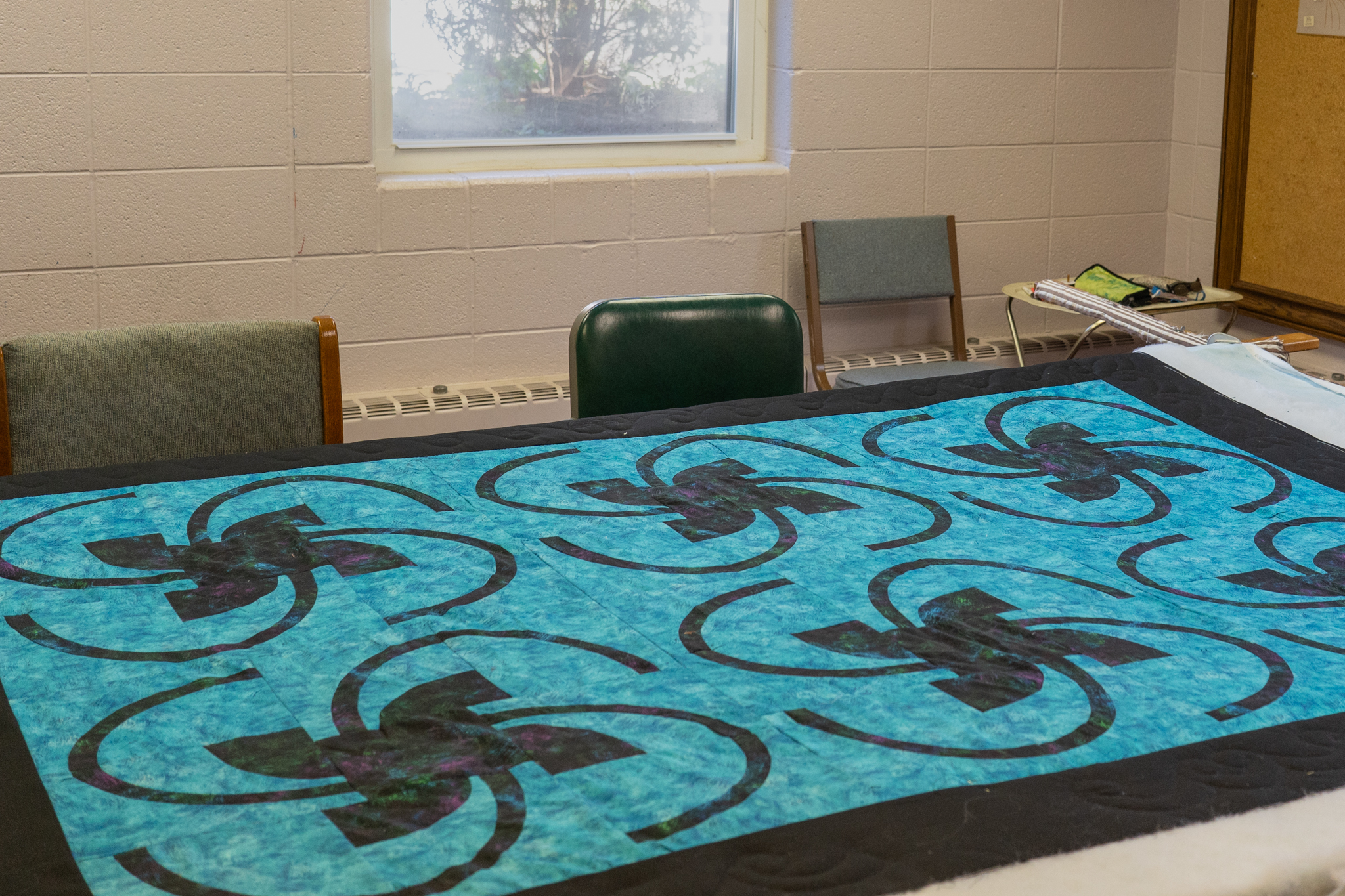 A quilt in progress with a teal background, black border, and a black swirl quilted pattern.