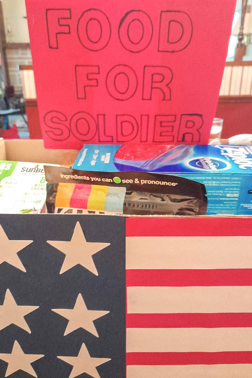 A box containing donations with an American flag on the front and a sign reading "food for solider"